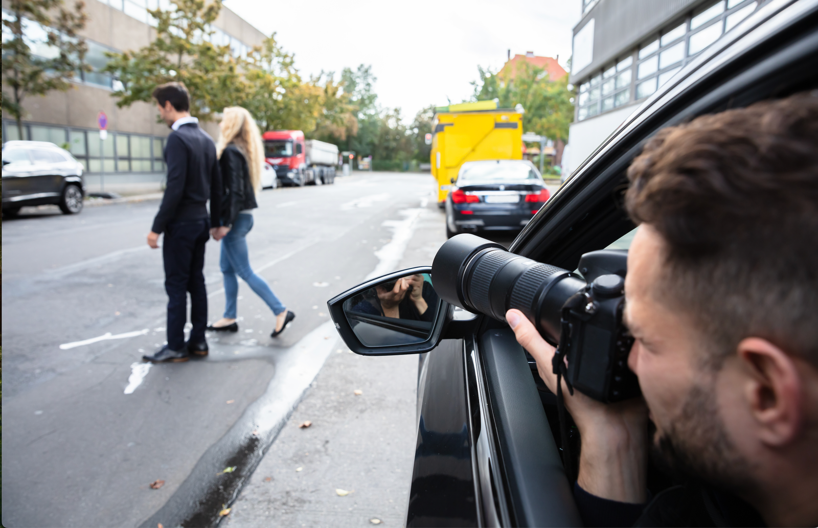 man in car secretly taking photos of man and woman walking across the street